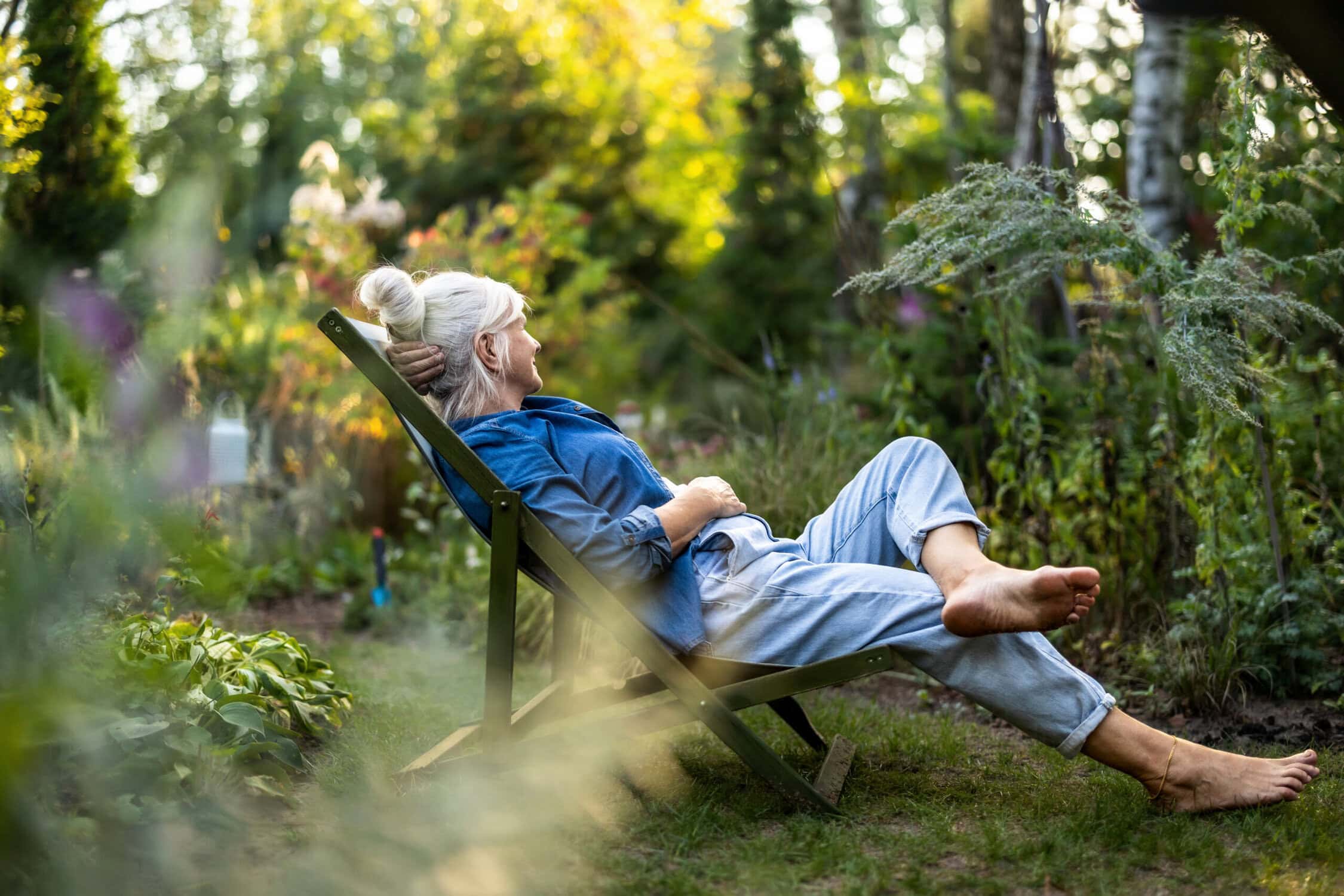 Rustende vrouw in tuin op ligstoel, ontspannen en genieten van de natuur.