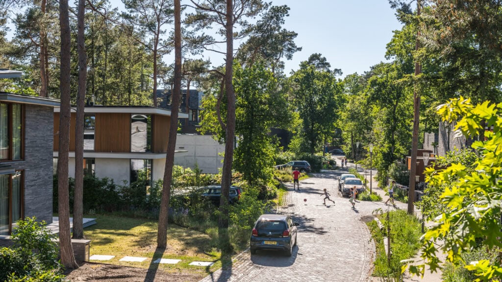 Moderne architectuur van de Vliegbasis W210 omgeven door groen, met een rustig straatbeeld en kinderen die spelen, onderstreept de harmonieuze combinatie van militaire faciliteiten en natuur.