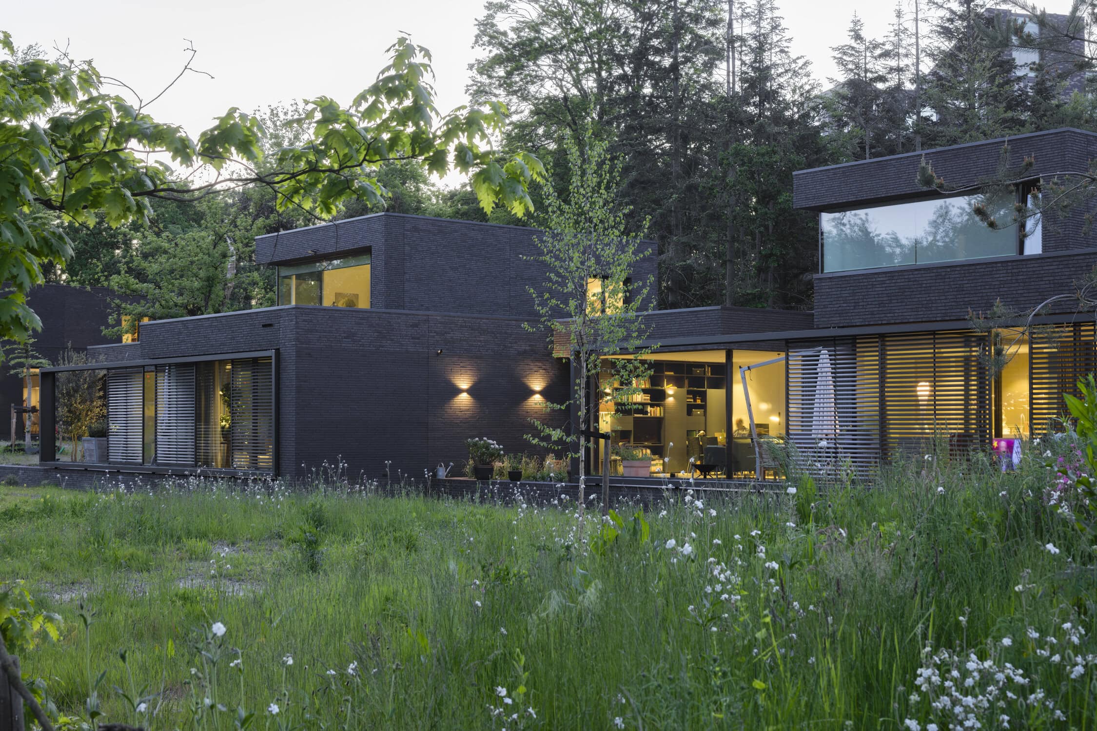 Modern ontworpen woning met grote ramen in een groene omgeving.