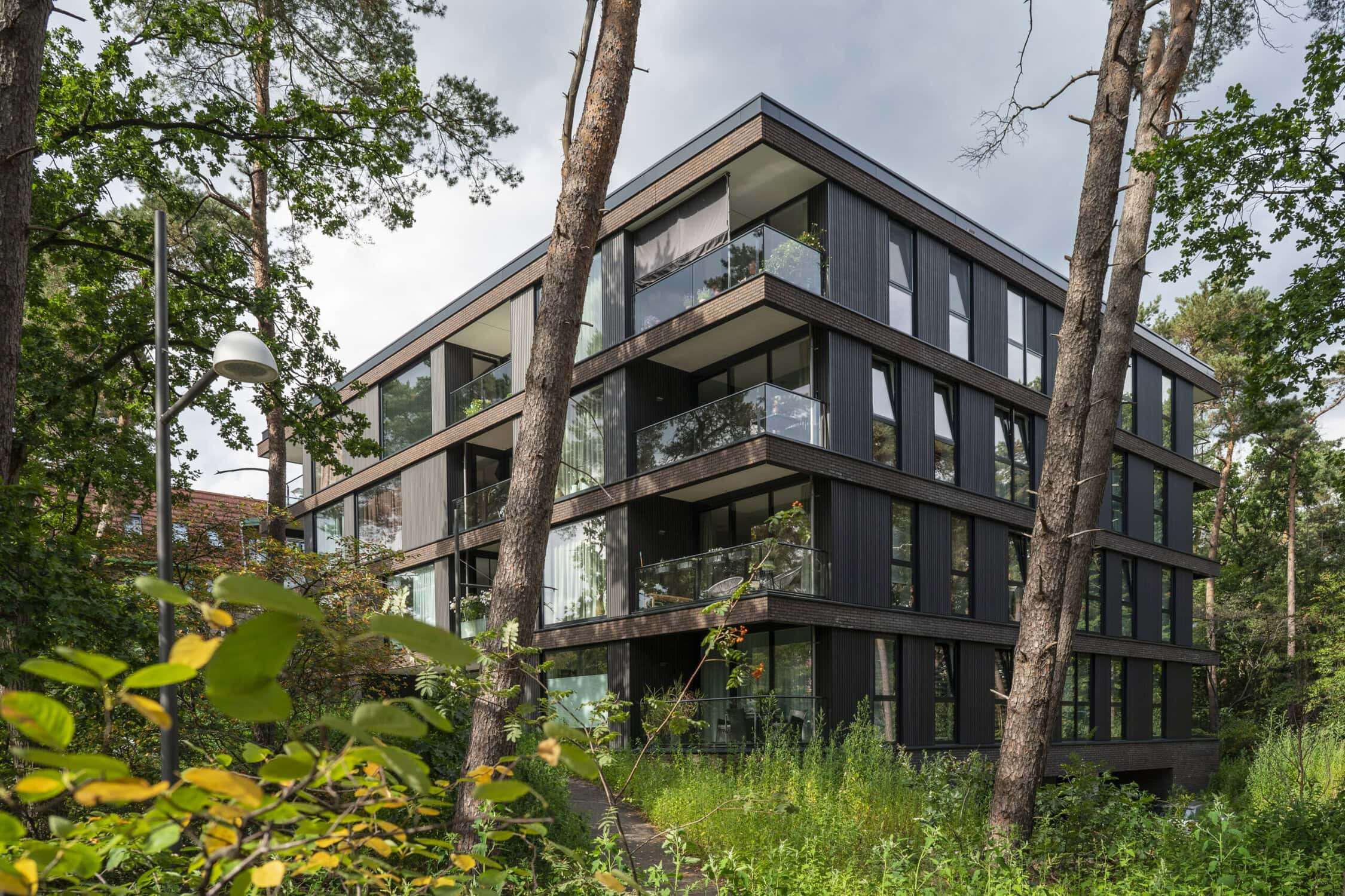 Modern appartementengebouw in bosrijke omgeving met grote glazen ramen en balkons, omgeven door bomen en groen, architectonisch design, duurzaam wonen, natuur en comfort.