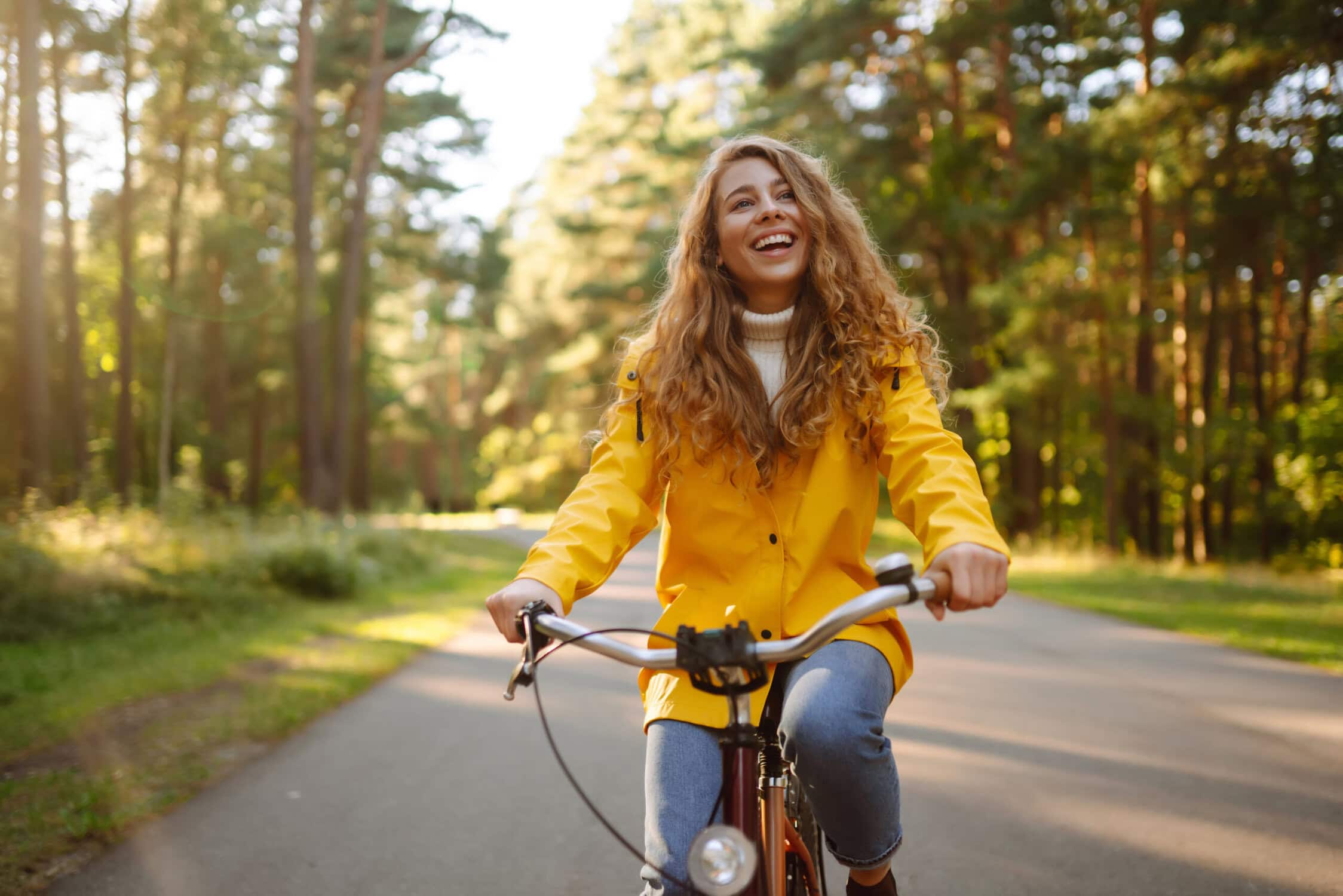 Vrolijke vrouw fietst door bosrijke omgeving in de herfst met een gele jas.