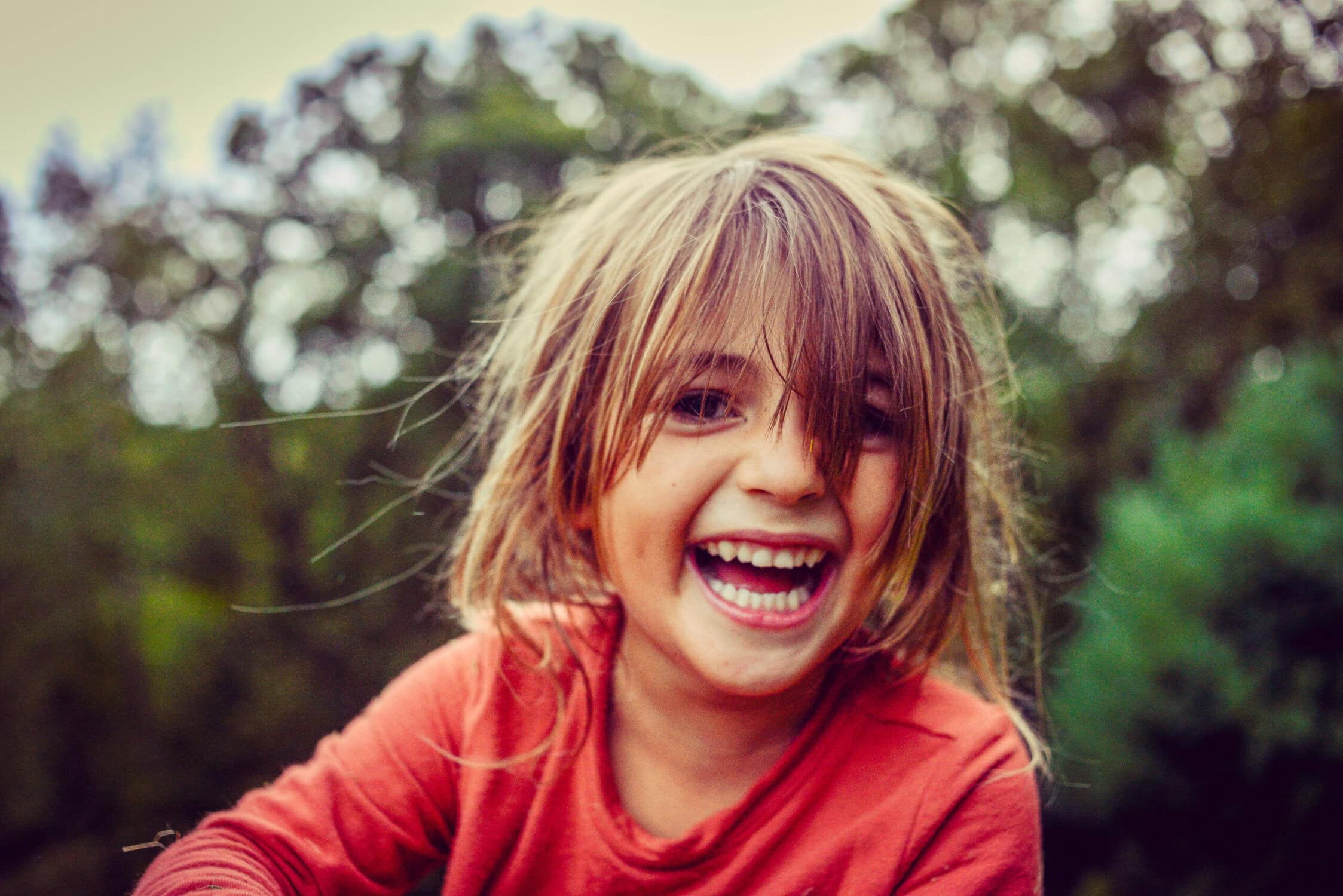 Vrolijk kind met nat haar glimlachend in de buitenlucht, in een groene natuurlijke omgeving.