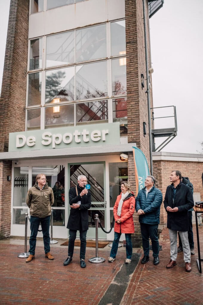 Werk aan de Vliegbasis De Vliegbasis, modern gebouw met glazen gevel, opening of evenement, geïnspireerd door de luchtmacht en militaire geschiedenis, symboliseert innovatie en samenwerking.