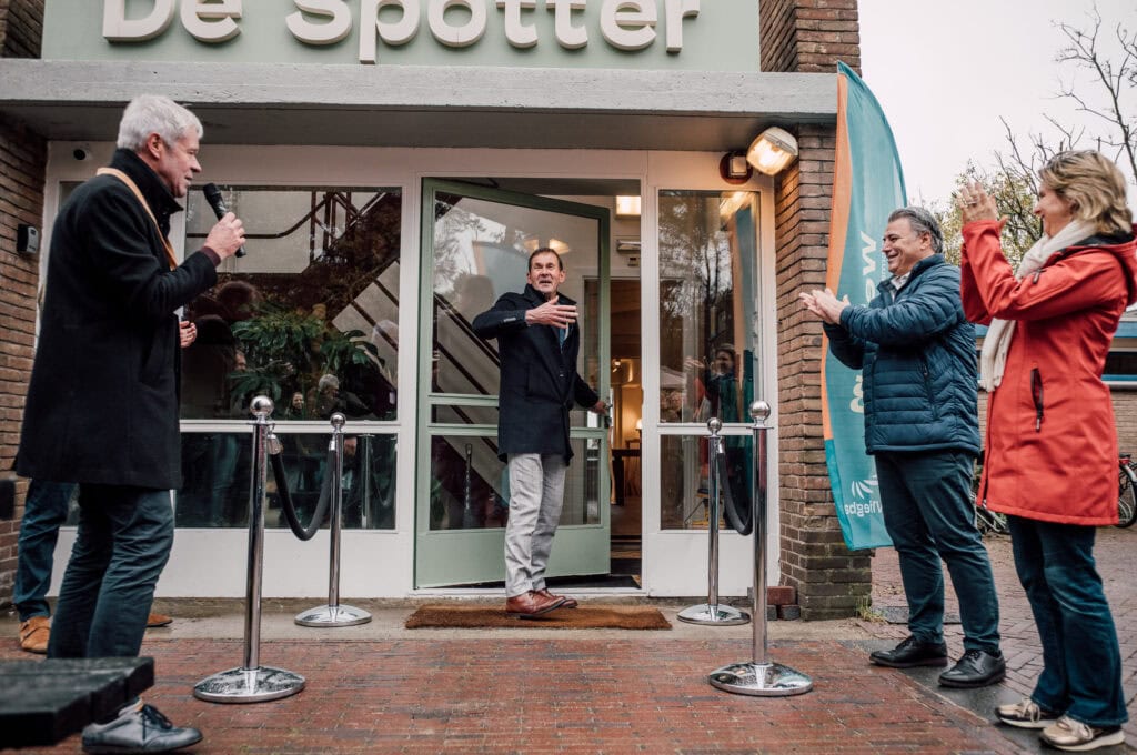 Moderne de Vliegbasis, herinnert aan militaire geschiedenis, met een feestelijke opening en gasten die applaudisseren buiten het gebouw, strategisch gelegen op de voormalige vliegbasis.