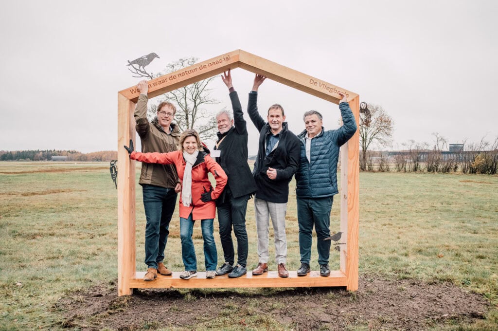 Unieke houten poort met luchtvaartmotto voor Vliegbasis, omgeven door natuur, met lancering van nieuwe symboliek ter promotie van de luchtmacht en natuurbehoud op de vliegbasis.