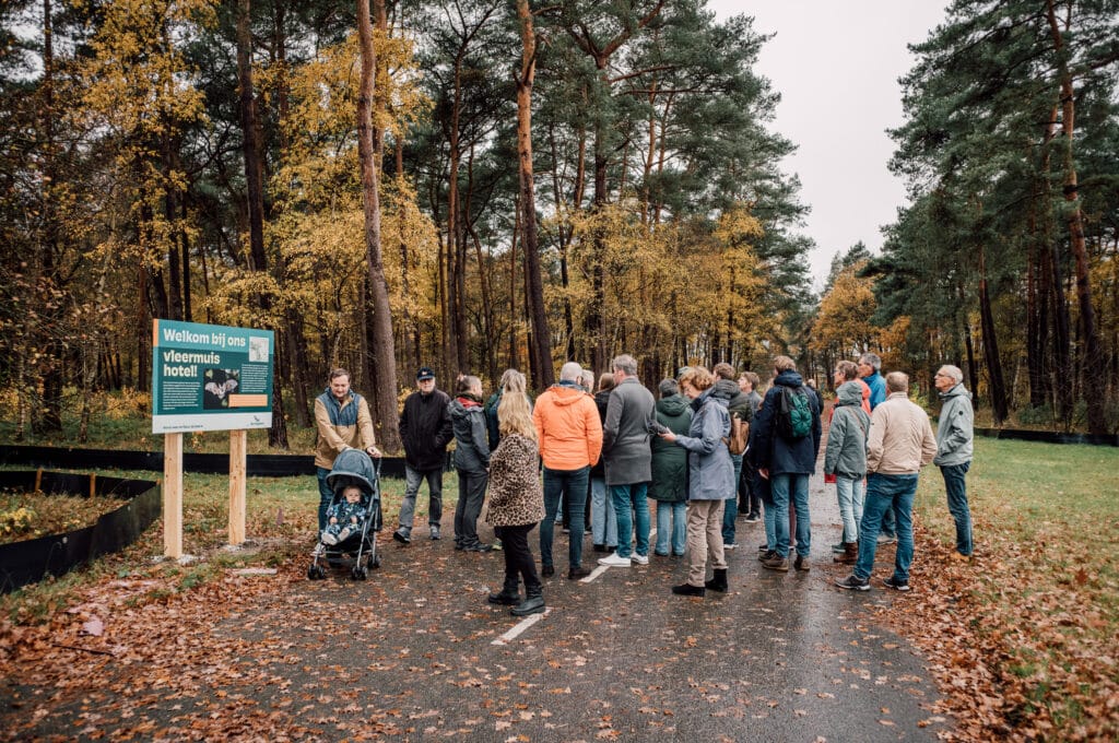 Grote groep bezoekers bij de Vliegbasis in een bosrijke omgeving tijdens een rondleiding of evenement.
