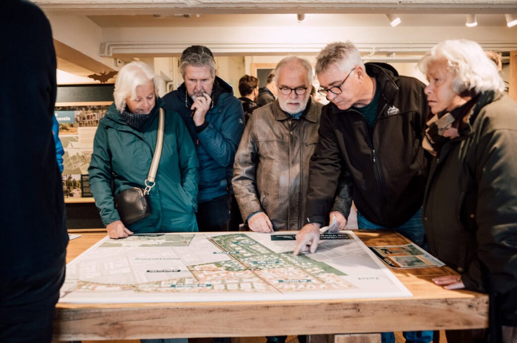 Ontwerpers van de Vliegbasis bekijken een gedetailleerde plattegrond tijdens een informatiesessie.