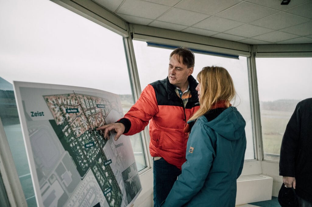 Moderne luchtmachtbasis met informatiescherm, uitleg over het vliegveld en strategische planning, mensen in gesprek bij de Vliegbasis, overzicht van de locatie en infrastructuur.