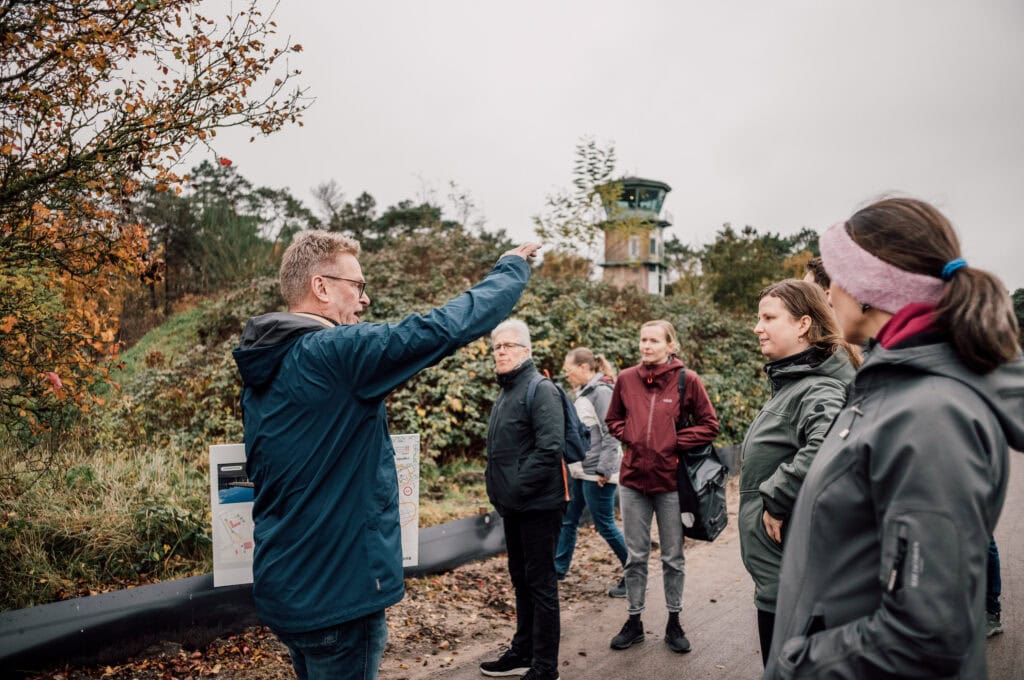 Elevatietekst, begeleide excursie op de Vliegbasis, gids vertelt aan groepsleden over militaire geschiedenis en luchtvaart tijdens een educatieve outdoor activiteit.