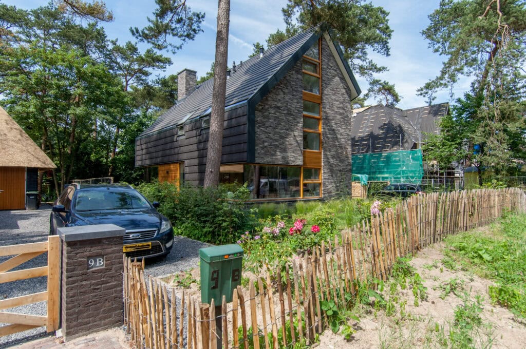 Luxe moderne bosvilla met grote ramen en houten gevel, gelegen op een rustige locatie nabij de Vliegbasis, omgeven door groen en natuur.