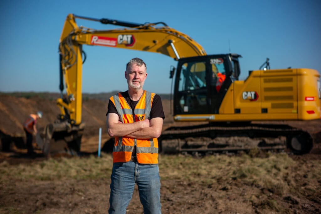 Man in veiligheidsvest voor bouwmachine op Vliegbasis, actief in bouwprojecten.